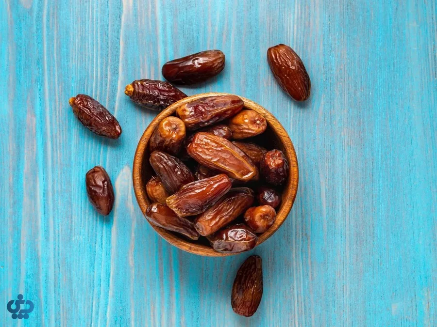خرمای تازه در کاسه چوبی روی پس‌زمینه آبی