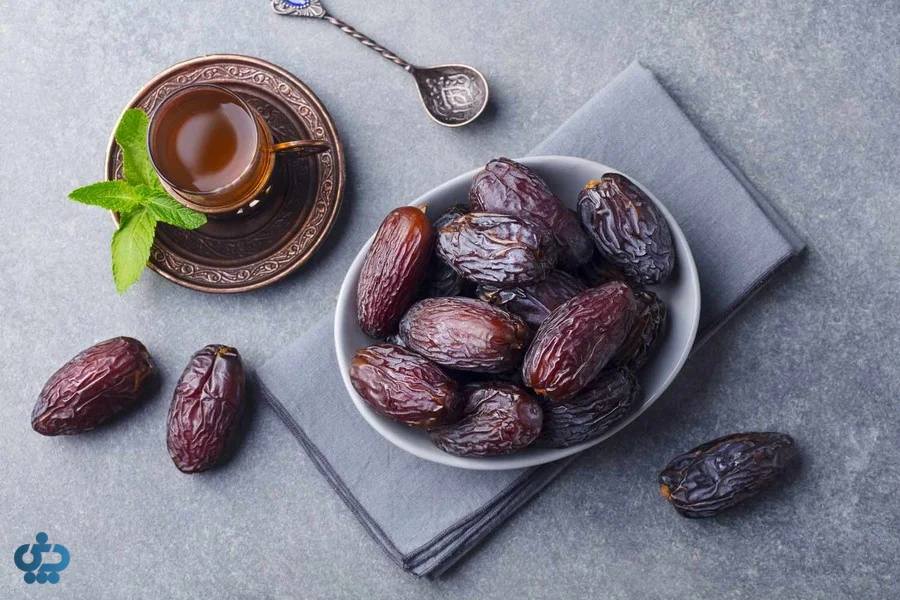 خرمای مجول در ظرف سفید در کنار چای و برگ نعناع
